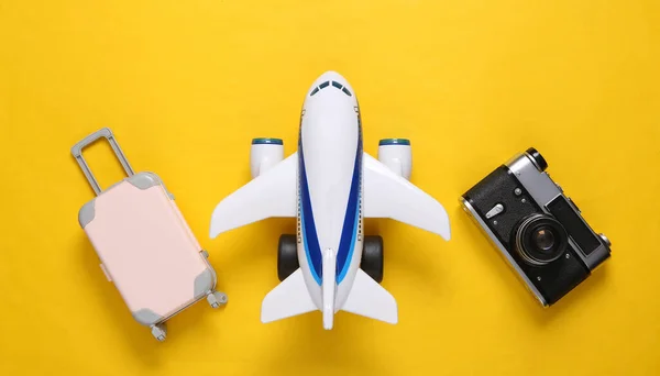 Travel flat lay. Toy passenger plane, camera and luggage on yellow background. Top view