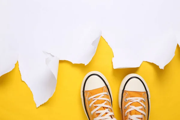 Retro classic sneakers (rubber shoes) and white torn paper sheet on yellow background. Copy space. Top view