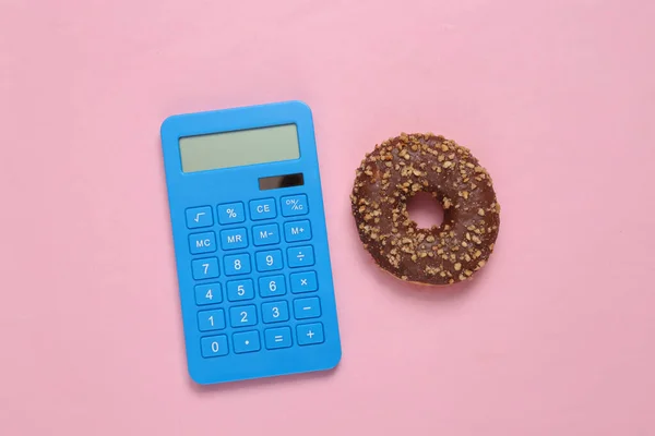 Calorie counting. Calculator and high calorie donut on pink background