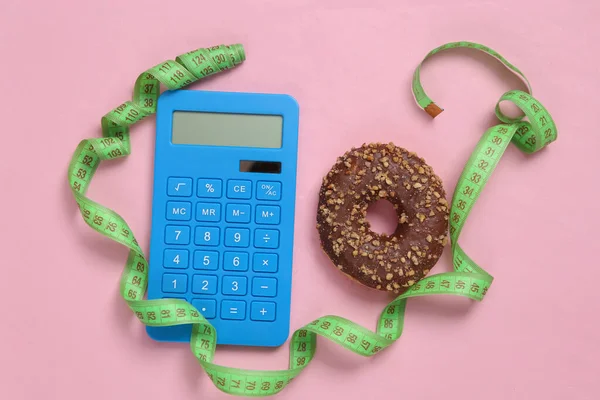 Calorie counting. Calculator and measuring tape, high calorie donut on pink background
