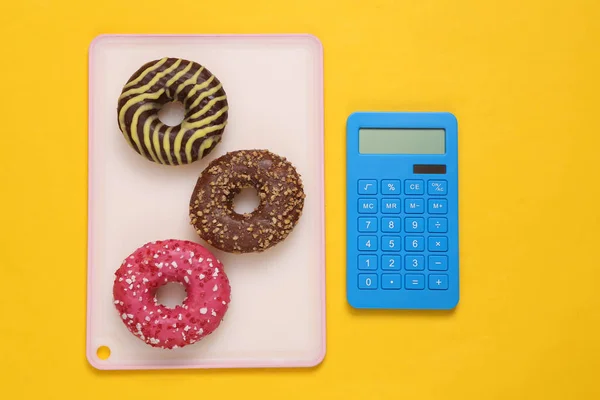 Calorie counting. Calculator and high calorie donuts on yellow background
