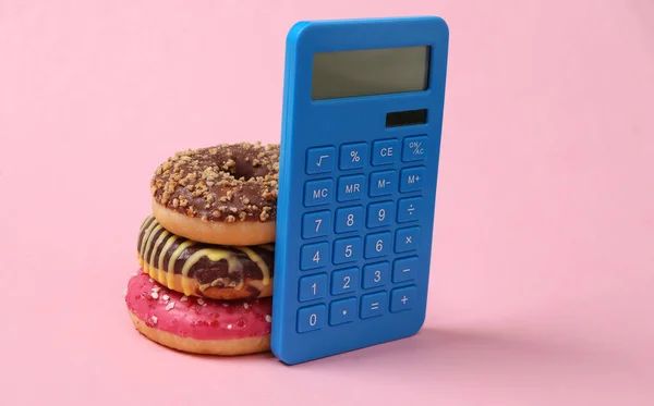 Calorie counting. Calculator and high calorie donuts on pink background