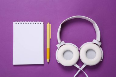 Stereo kulaklıklar ve mor arka planda fotokopi için boş bir defter. Fitness konsepti. Eğitim planı