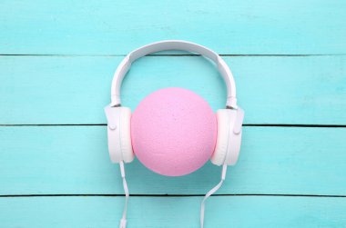 Mavi ahşap arka planda pembe topa takılan kulaklıklar. Yaratıcı düzen. Minimalizm müzik konsepti 