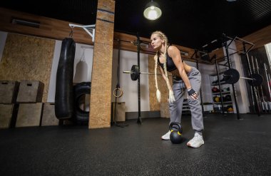 Modern spor salonunda kettlebell ile yapılan yoğun eğitimden sonra yorgun ve zinde bir kadın dinleniyor. Fonksiyonel eğitim
