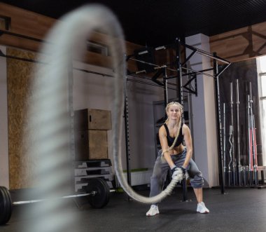 Atletik güçlü kadın modern spor salonunda savaş halatıyla egzersiz yapıyor. Fonksiyonel eğitim