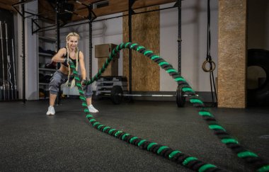 Atletik güçlü kadın modern spor salonunda savaş halatıyla egzersiz yapıyor. Fonksiyonel eğitim