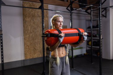 Atletik güçlü kadın modern spor salonunda ağır çalışma çantasıyla egzersiz yapıyor. 