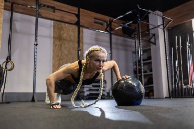 Modern spor salonunda tıp topuyla şınav çeken atletik bir kadın.