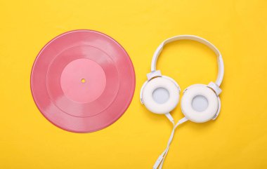 Yaratıcı müzik düzeni. Sarı arka planda pembe plak ve kulaklık. Minimalizm. Düz yatıyordu. Üst görünüm.