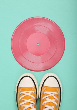 Yaratıcı retro 80 'lerin düzeni. Pembe vinil plak ve nane mavisi arka planda spor ayakkabı. Minimalizm. Düz yatıyordu. Üst görünüm.