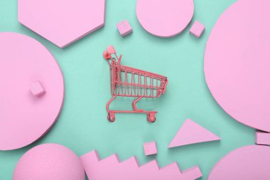 Yaratıcı alışveriş düzeni. Nane mavisi arka planda pembe farklı geometrik şekillere sahip pembe süpermarket arabası. Pastel renk eğilimi. Minimalizm. Sanat kavramı. Düz yatıyordu. Üst görünüm.