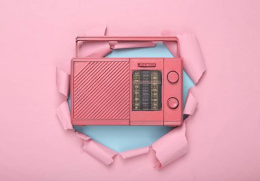 Yaratıcı müzik düzeni. Pembe analog radyo alıcısı yırtık pembe kağıt deliğinden geçiyor. Minimalizm. Sanat kavramı. Düz yatıyordu. Üst görünüm.