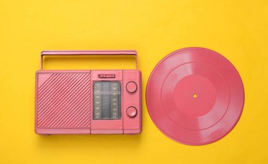 Pembe havalı radyo alıcısı ve sarı arka planda vinil plak. Minimal müzikal konsept. Üst Manzara. Düz yatıyordu