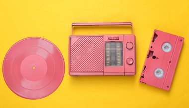 Pembe havalı radyo alıcısı, video kaset ve sarı arka planda vinil plak. Minimal müzikal konsept. Üst Manzara. Düz yatıyordu