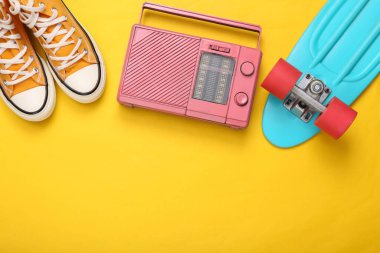 Sarı arka planda geçmişe dönük hipster özellikleri. Bozuk para panosu, radyo ve spor ayakkabıları. Minimalizm, yaratıcı düzen. Düz yatıyordu. Sanat kavramı. Pastel renk eğilimi. Üst Manzara. Boşluğu kopyala