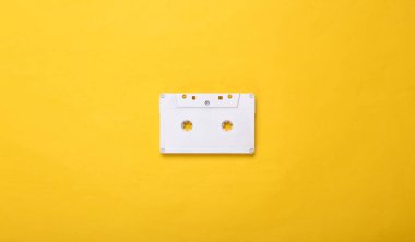 Yaratıcı müzik düzeni. Sarı arka planda beyaz retro ses kaseti. Pastel renk eğilimi. Minimalizm. Sanat kavramı. Modern natürmort. Düz yatıyordu. Üst görünüm.
