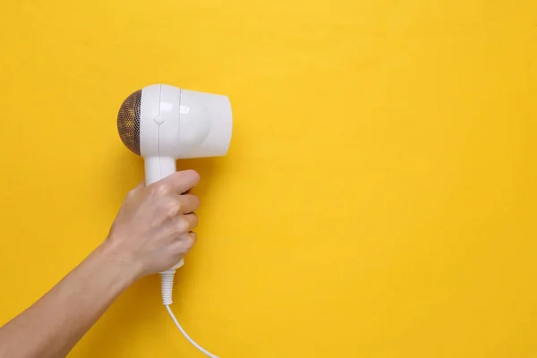 stock image Hand holding White hair dryer on yellow background. Beauty concept. Hair care, hair style. Top view. Flat lay. Copy space