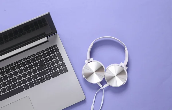 Laptop with headphones on purple background. Musical concept. Top view