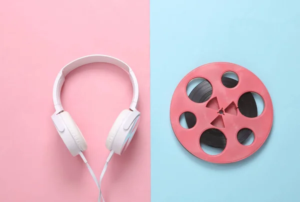 Pink retro audio reel and headphones on blue pink background. Minimalism music concept. Top view