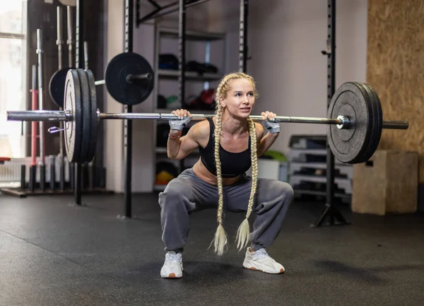 Modern spor salonunda omuzlarında ağır halterlerle çömelmiş genç bir kadın. İşlevsel, kas çalıştırıcı bacaklar ve kalçalar. 