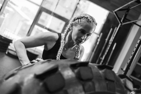适合女运动员翻动巨大的轮胎 女人举起了一个沉重的轮子 肌肉发达的年轻女子在体育馆进行功能性训练 — 图库照片