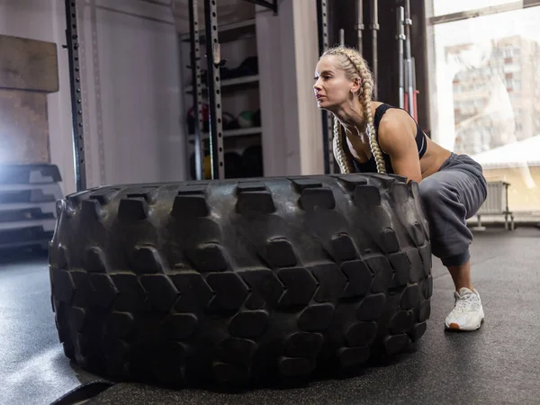 Fit female athlete flipping huge tire. Woman lifts a heavy wheel. Muscular young woman doing functional training exercise at gym.