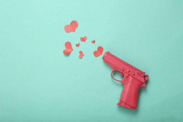Love layout made with pink gun firing red heart on mint blue background. Creative valentines or romantic concept. Flat lay, top view.