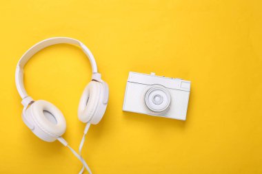 Sarı arka planda kamera olan beyaz kulaklıklar. Yaratıcı düzen. Üst Manzara. Düz yatıyordu