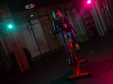 Güzel, genç, formda bir kadın spor salonunda staj bisikletinde pembe yeşil neon ışık gradyan ışıklarıyla kardiyo yapıyor. Spor, spor, yaşam tarzı konsepti