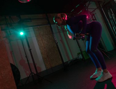 Spor salonunda elinde dambıllarla spor yapan zayıf, genç, formda bir kadın. Spor, spor, yaşam tarzı konsepti