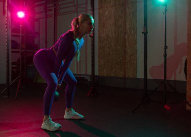 Genç, sıska kadın ellerinde kettlebell olan kasları jimnastik salonunda pembe yeşil ışıkla eğitiyor. Spor, spor, yaşam tarzı konsepti
