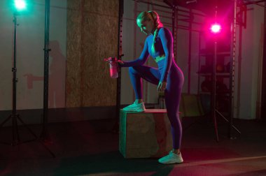 Fitness modeli dinlenme, spor salonunda pembe yeşil neon ışıklı su içme. Spor, spor, yaşam tarzı konsepti