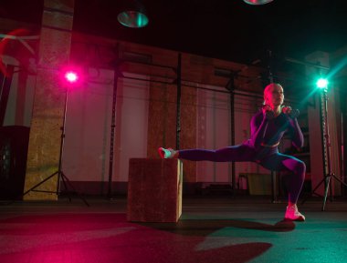 Dambılı kaslı kadın modern spor salonunda ahşap kutuda hareketlenmeye çalışıyor. Spor, spor, yaşam tarzı konsepti.