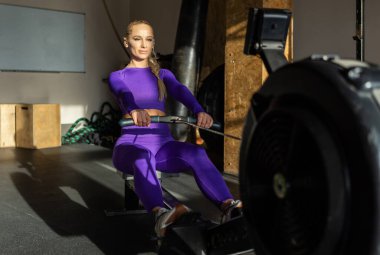 Bir kadın spor salonunda kürek çekme makinesinde kardiyo çalışması yapıyor. Sportif kız fitness kulübünde çalışıyor. Sağlıklı yaşam tarzı