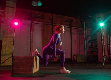 Dambılı kaslı kadın modern spor salonunda ahşap kutuda hareketlenmeye çalışıyor. Spor, spor, yaşam tarzı konsepti.