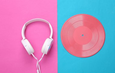 Yaratıcı müzik düzeni. Mavi-pembe arka planda Stereo kulaklıklar ve vinil plak. Üst manzara, düz yatış. Sanat kavramı