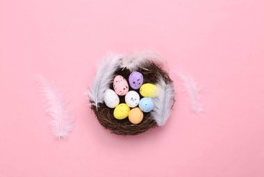 Yuvadaki renkli yumurtaların ve pembe arka plandaki tüylerin Paskalya kompozisyonu. Üst Manzara. Düz yatıyordu