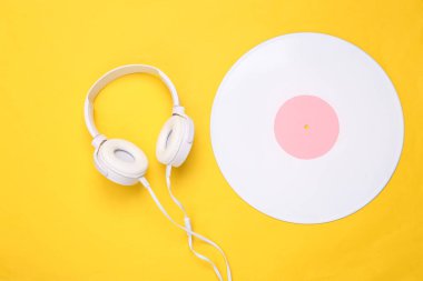 Yaratıcı müzik düzeni. Sarı arka planda beyaz plak ve kulaklık. Üst Manzara. Düz yatıyordu