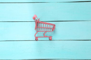 Yaratıcı Alışveriş Planı. Mavi ahşap arka planda pembe alışveriş arabası. Minimalizm. Üst Manzara. Düz yatıyordu