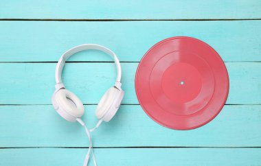 Yaratıcı müzik düzeni. Pembe plak kaydı ve mavi ahşap arka planda beyaz kulaklık. Minimalizm. Üst Manzara. Düz yatıyordu