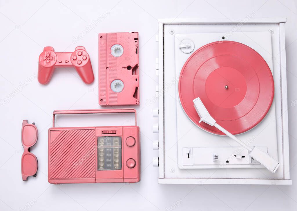 Retro creative layout. White vinyl record player, pink gamepad, video cassette, glasses, radio on a white background. Top view. Flat lay