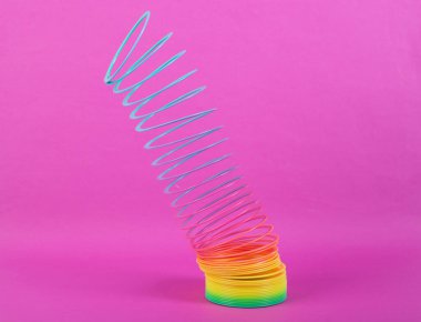 Pembe arka planda gerilmiş Gökkuşağı plastik, çok renkli spiral, ince çizgili oyuncak. Minimalizm