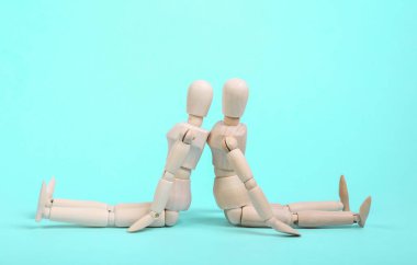 Kavgadaki tahta kuklalar mavi arka planda sırt sırta otururlar.