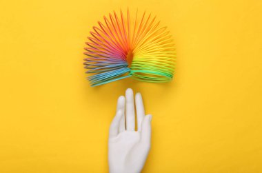 Beyaz el ve sarı arka planda Gökkuşağı Plastik, çok renkli spiral, ince çizgili oyuncak. Minimalizm
