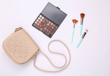 Kadın aksesuarları. Beyaz arka planda güzellik ürünleri. Göz farı paleti, makyaj fırçası ve çanta. Üst görünüm
