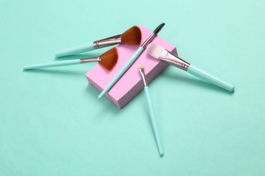 Minimalist güzellik sahnesi. Mavi arka planda pembe platformlu makyaj fırçaları. 