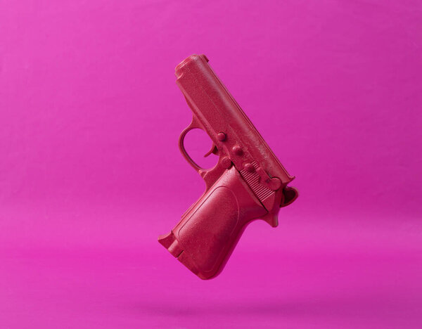 Levitating pink gun on pink background. Minimalistic still life. Creative layout. Concept art