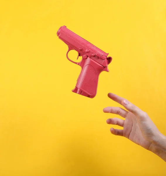Hand and Levitating pink gun on yellow background. Minimalistic still life. Concept art. Video game