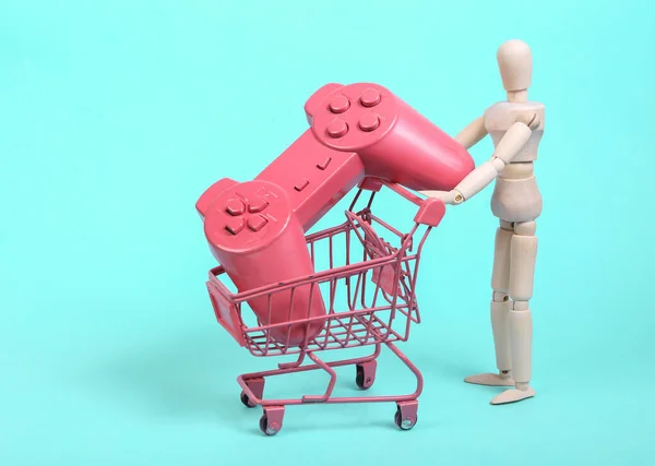 青い背景にゲームパッド付きミニショッピングトロリーを保持人形 ショッピングのコンセプト — ストック写真